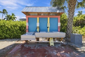 A small, single-room structure with a corrugated metal roof and a wooden front panel. There are two sinks and a bench in front of the room.