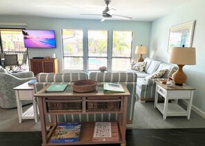 A living room with a sofa, a coffee table with books, a television, and a window with blinds.