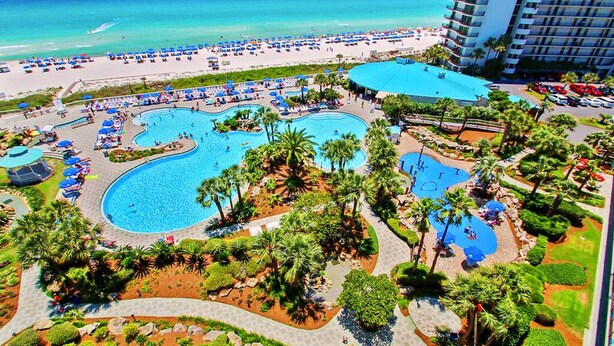 Un resort con varias piscinas, una playa y un amplio edificio de hotel.