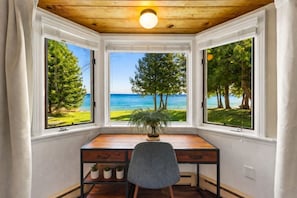 Ein Zimmer mit Schreibtisch, Stuhl und Meerblick durch große Fenster.