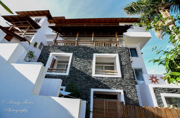 Un edificio moderno con fachada de piedra, varios balcones y una pérgola de madera.