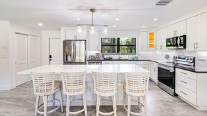 A modern kitchen with white cabinetry, stainless steel appliances, and a central island with bar stools.