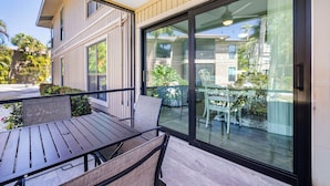 A balcony with a table and chairs, a sliding glass door, and a view of a building and greenery.