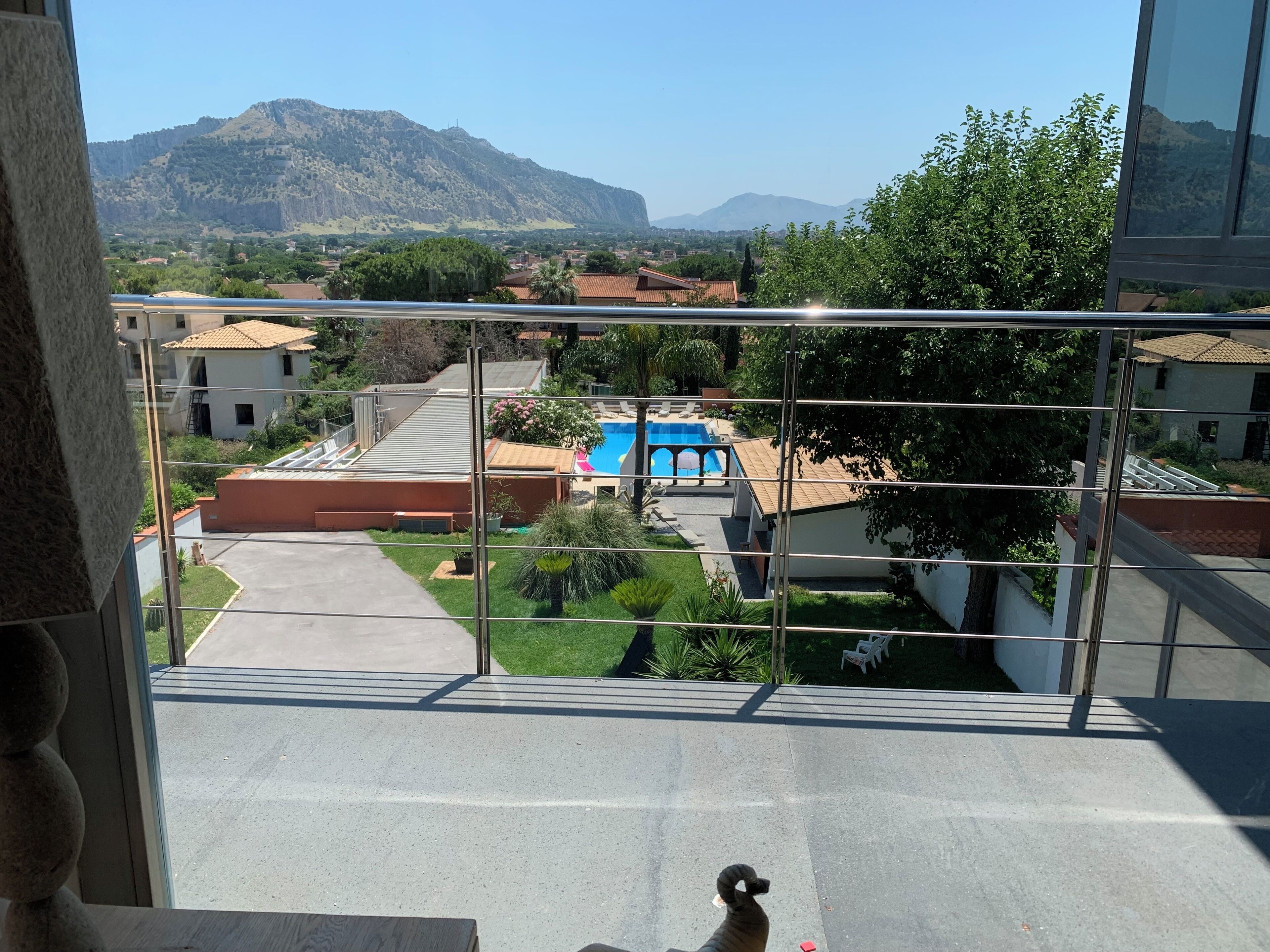 A balcony with a view of a residential area, a swimming pool, and distant mountains.