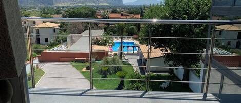 A balcony with a view of a residential area, a swimming pool, and distant mountains.