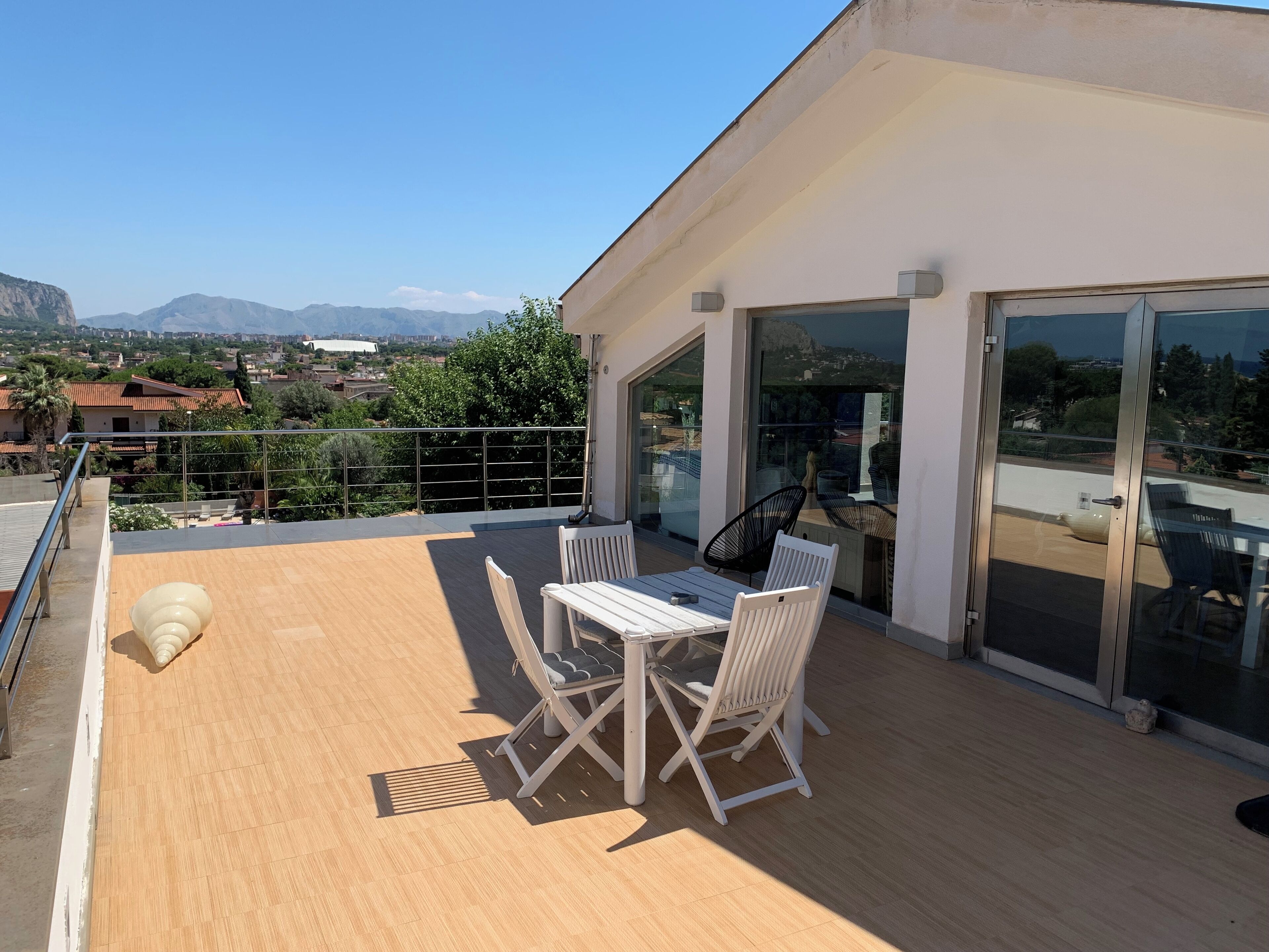 Un balcón moderno con una mesa, sillas, puertas de cristal y vistas a la ciudad y montañas.