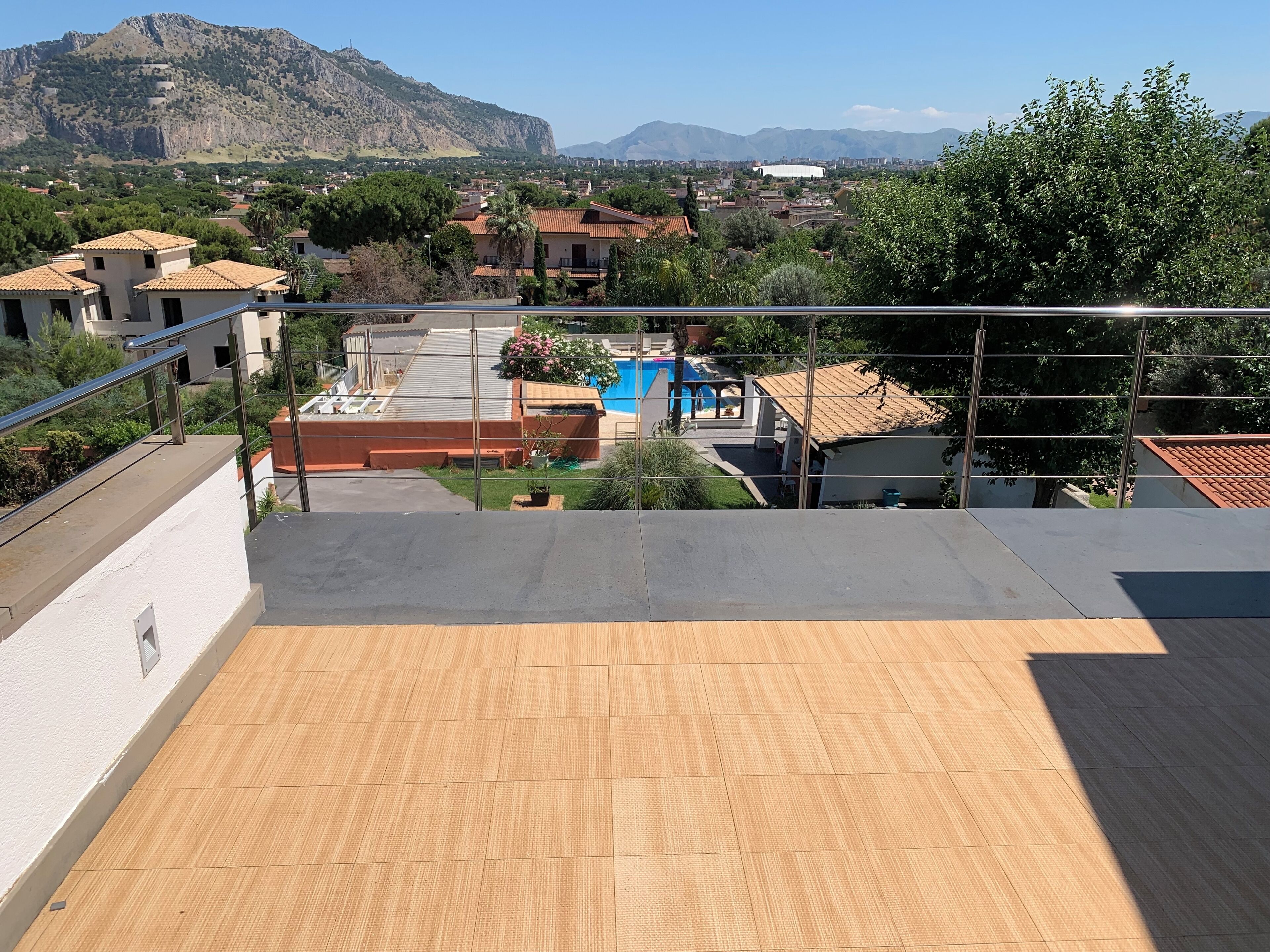A rooftop terrace with a view of a residential area, a swimming pool, and mountains in the background.