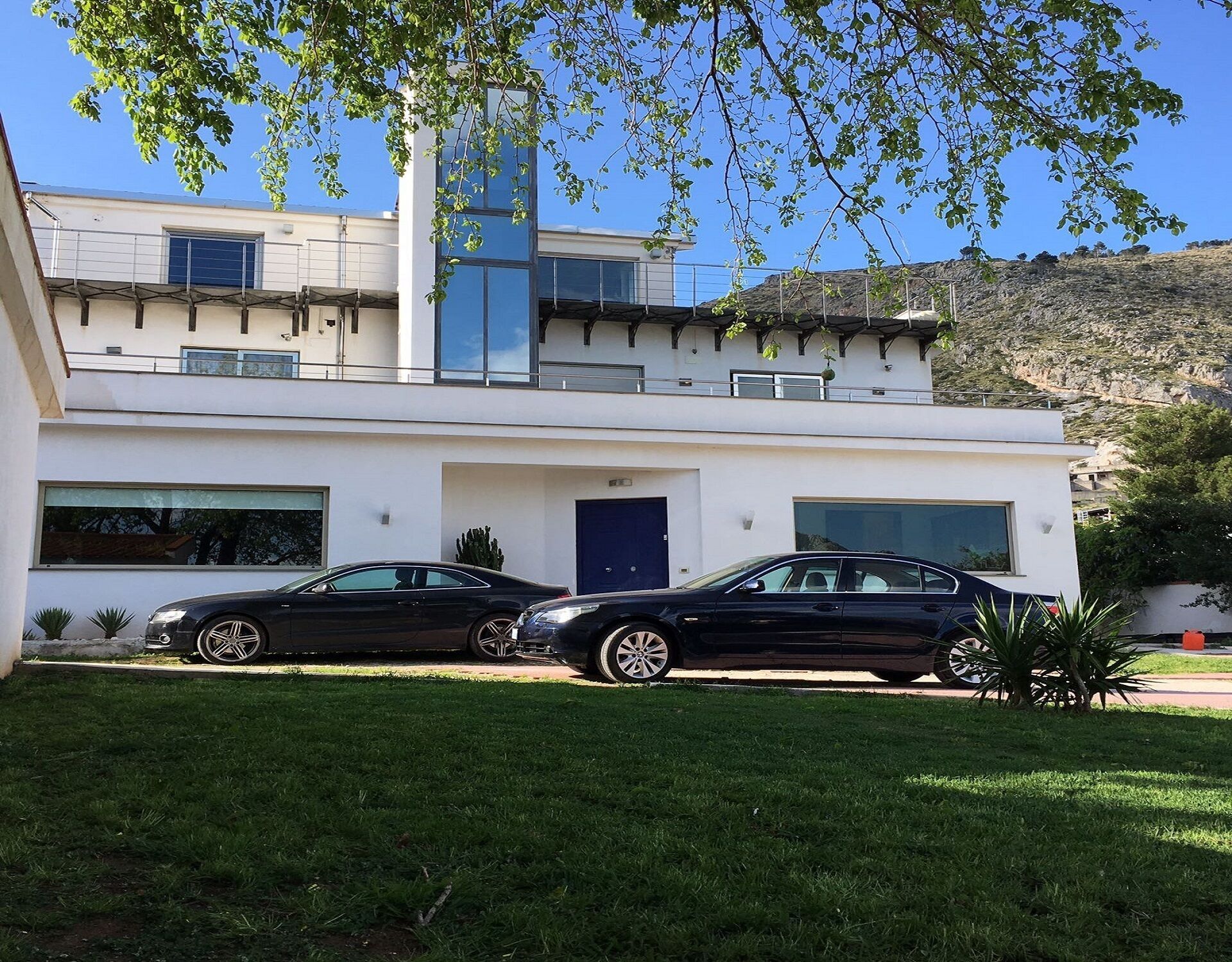 A modern two-story house with a garage, two cars parked in the driveway, and a well-maintained lawn.
