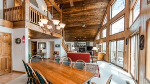 A spacious dining area with a wooden table and chairs, a balcony with a railing, and a fireplace in the background.