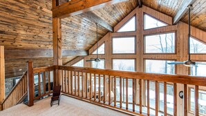 A wooden interior with a high ceiling, large windows, and a wooden railing.