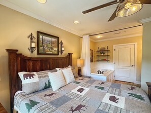 Une chambre à coucher avec une tête de lit en bois, un lit recouvert d’une courtepointe à motifs animaliers, une table de chevet avec une lampe, un tableau accroché au mur et une porte donnant sur une autre pièce.
