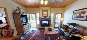 A living room with a fireplace, leather sofa, wooden entertainment unit, and a patterned rug.