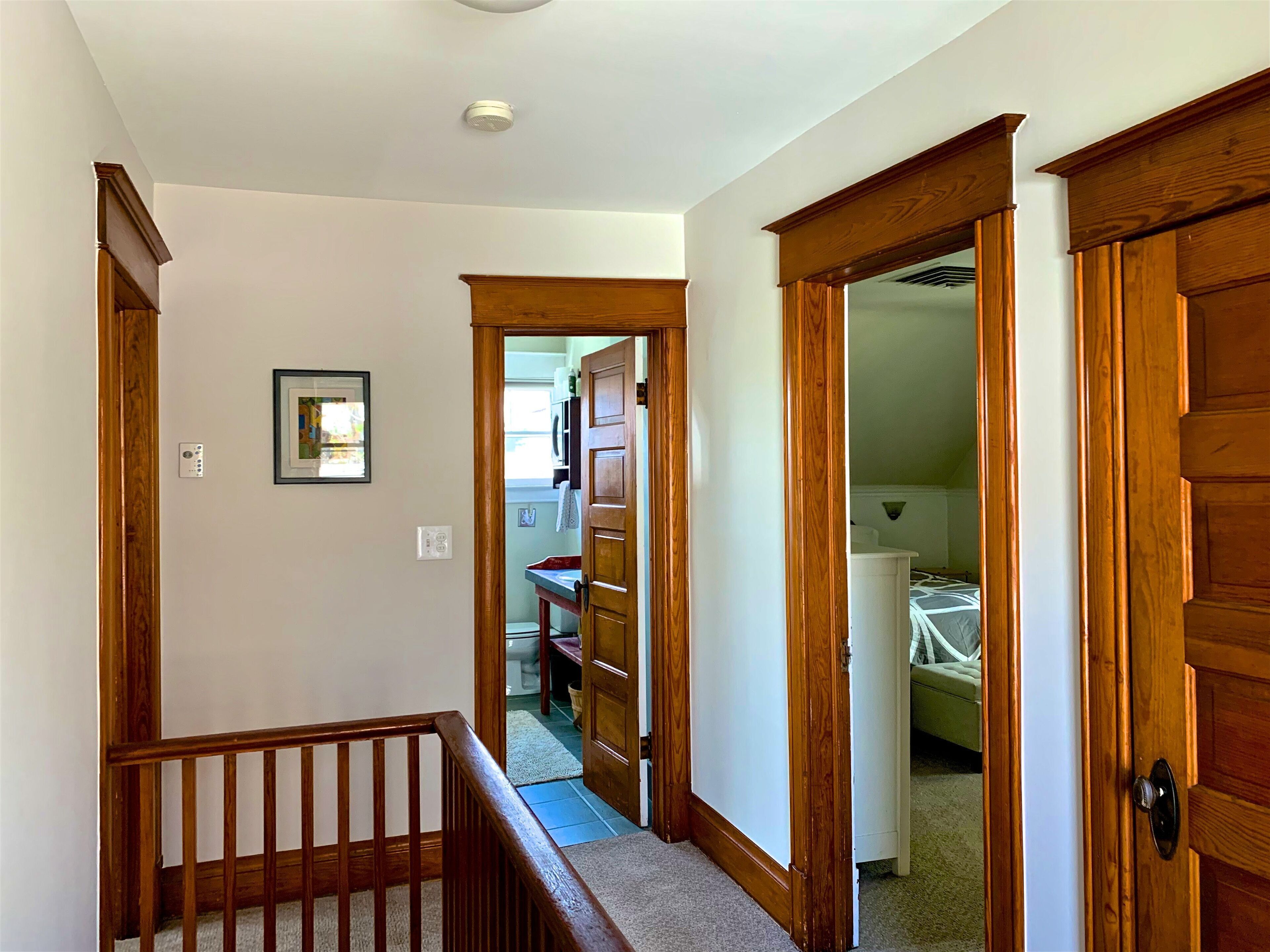 Un pasillo con puertas de madera, una escalera y un cuadro en la pared.
