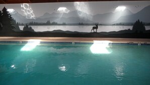 Piscina interna com um mural de paisagem montanhosa e um veado.
