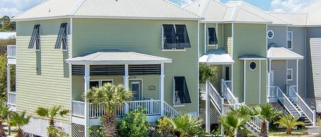 Una hilera de casas de playa de dos pisos, con balcones, un porche cubierto y suelo arenoso.