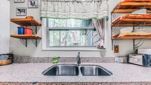 Una cocina con encimeras de granito, pileta doble, estantes de madera y una ventana con vista a árboles.