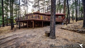 Una cabaña con terraza de madera, rodeada de altos pinos.