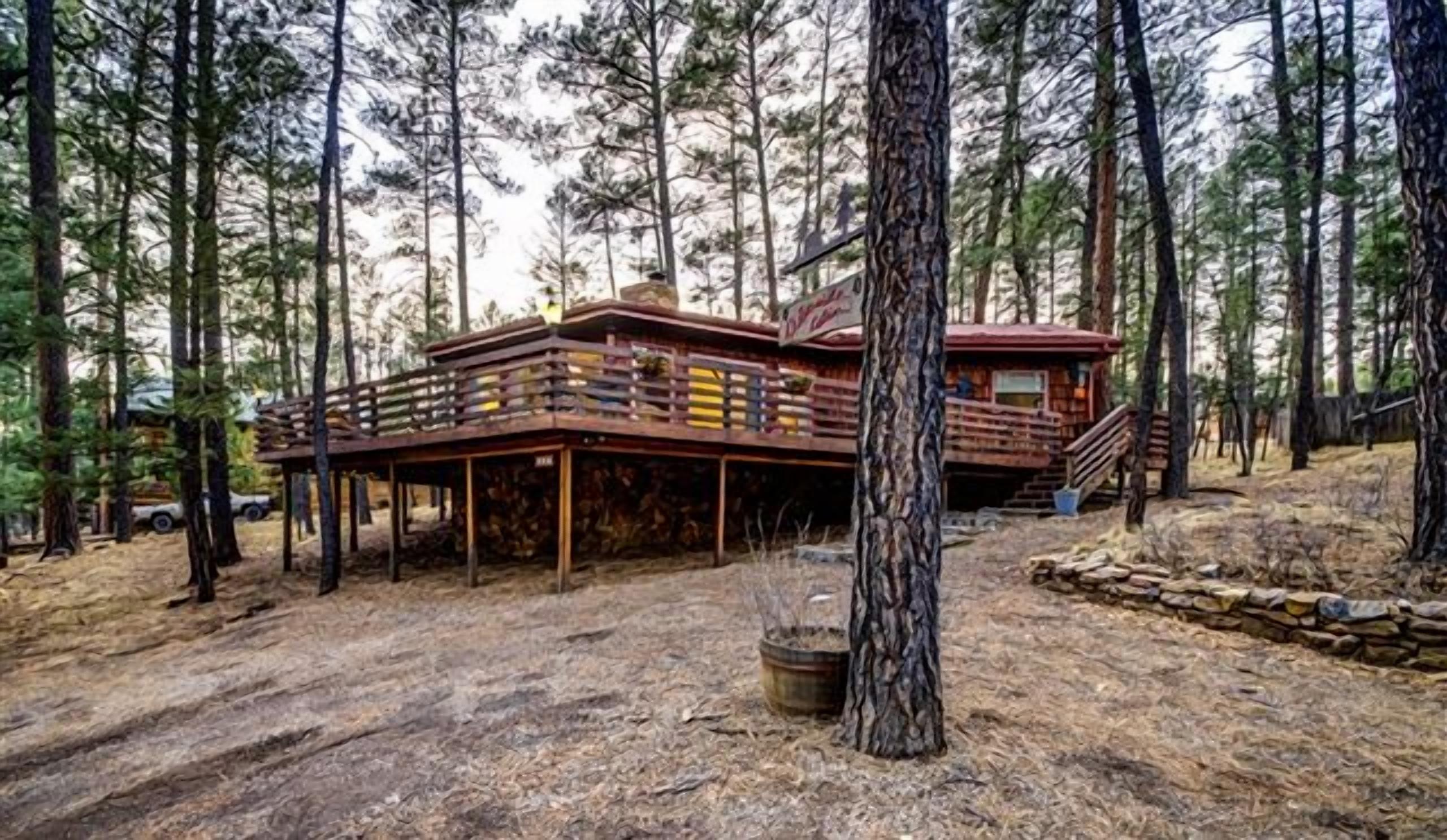 Una cabaña con terraza de madera, rodeada de altos pinos.