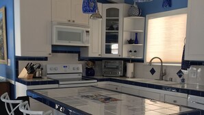 A modern kitchen with white cabinets, a central island with bar stools, a microwave, a toaster oven, and pendant lights. - OCEAN BREEZE BEACH HOME (Oxnard)