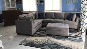 A living room with a sectional sofa, ottoman, and a patterned rug. - OCEAN BREEZE BEACH HOME (Oxnard)