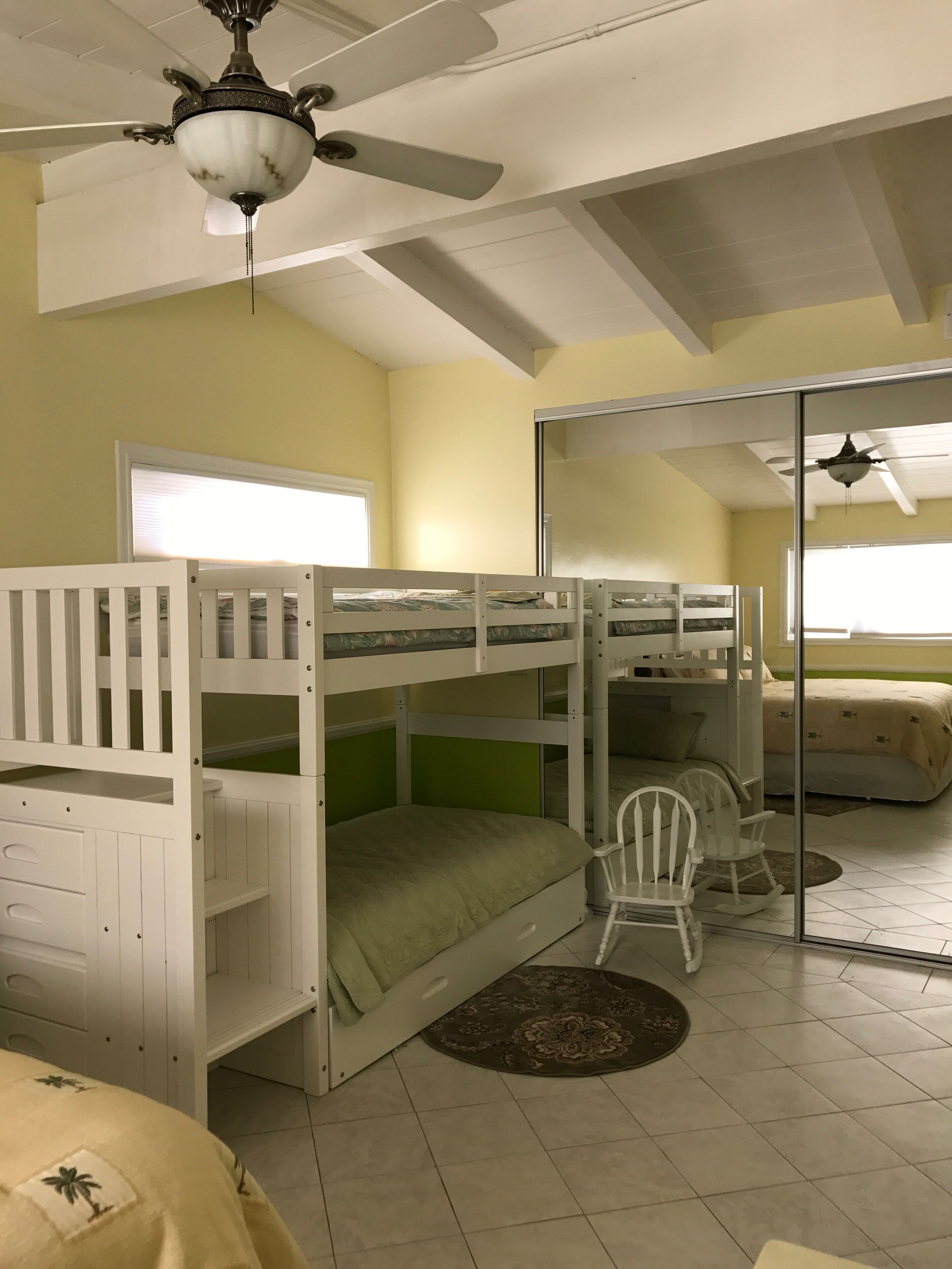 A room with bunk beds, a ceiling fan, a window, and a sliding glass door.
