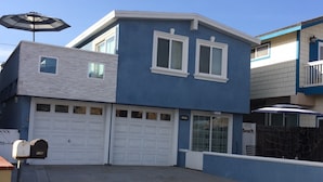 A two-story residential building with a garage, a small balcony, and a clear blue sky. - OCEAN BREEZE BEACH HOME (Oxnard)