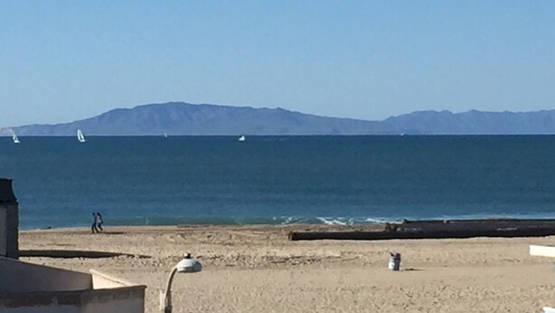 A beach with a clear view of the ocean and distant mountains. - OCEAN BREEZE BEACH HOME (Oxnard)