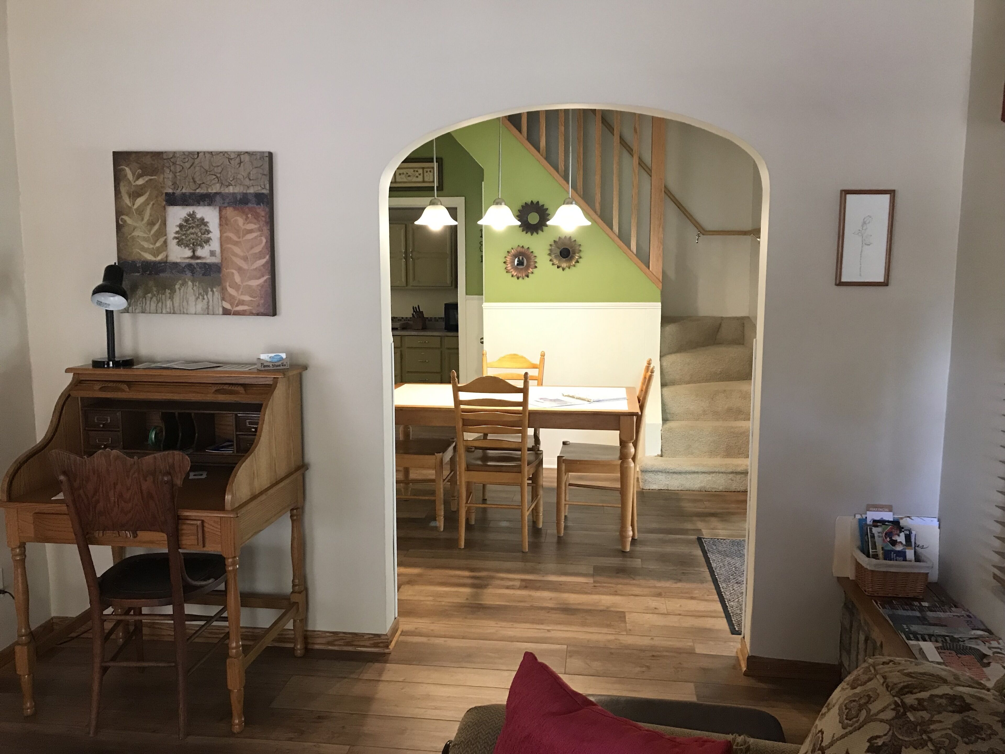 Un salon chaleureux avec un bureau en bois, une table à manger avec des chaises et un escalier menant à l’étage supérieur.