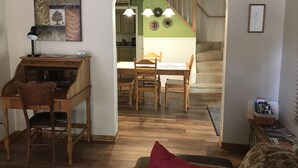 Un salon chaleureux avec un bureau en bois, une table à manger avec des chaises et un escalier menant à l’étage supérieur.
