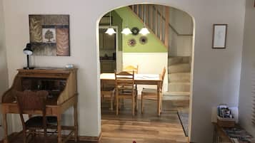Un salon chaleureux avec un bureau en bois, une table à manger avec des chaises et un escalier menant à l’étage supérieur.