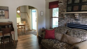 Un salon chaleureux avec une cheminée, un plancher en bois, un canapé et un coin repas comprenant une table et des chaises.