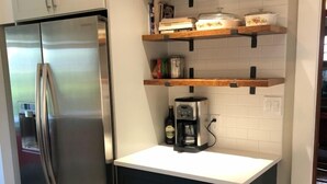 A compact kitchen with a stainless steel refrigerator, dark cabinetry, and wooden shelves above the countertop.
