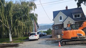 A residential street with a house, parked cars, and construction equipment.