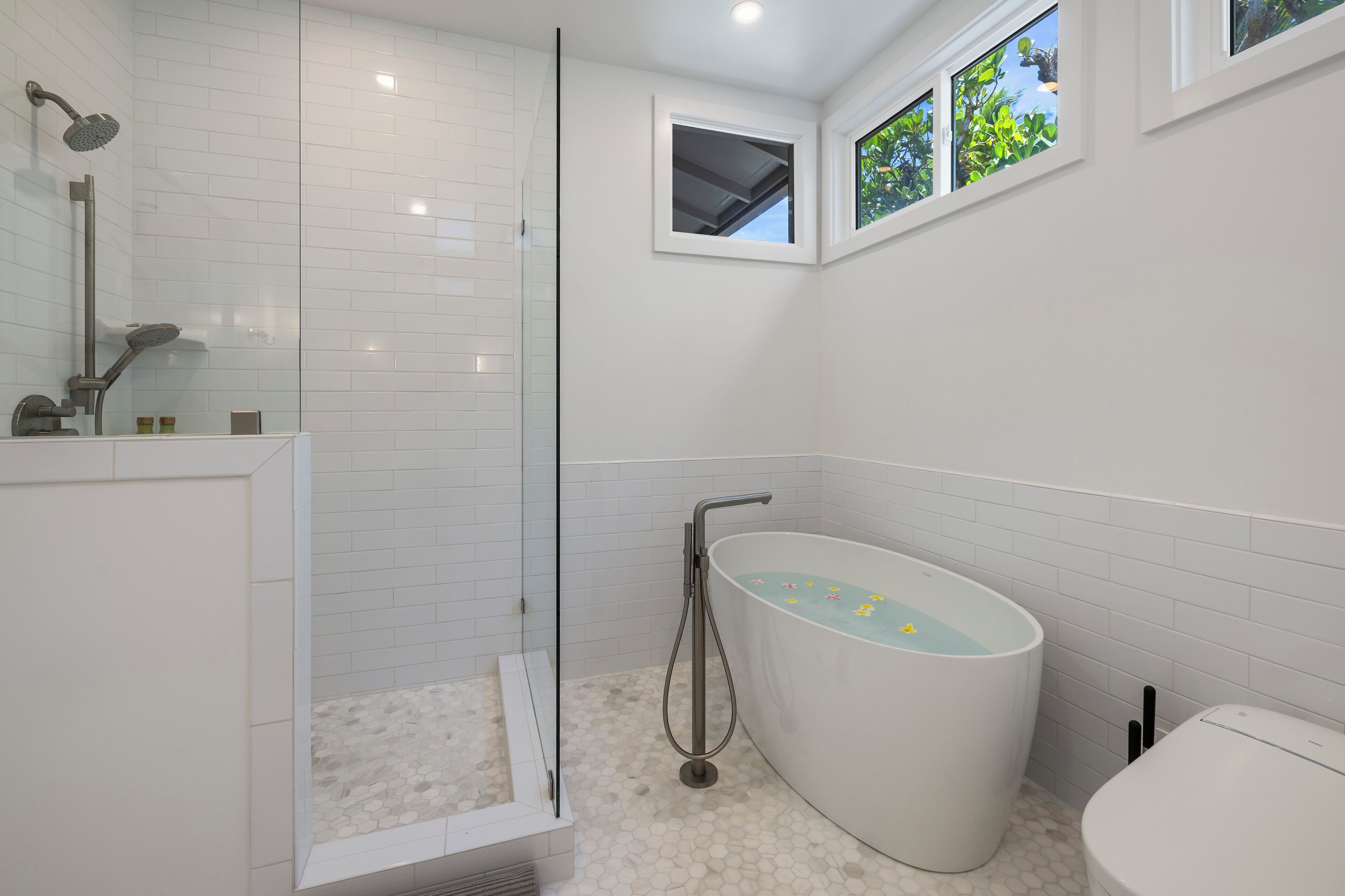 A modern bathroom with a glass-enclosed shower, a freestanding bathtub, and a toilet.
