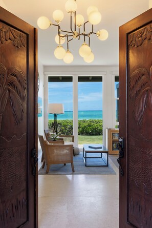 A room with a view of the ocean, a chandelier, and a wooden door with leaf carvings.