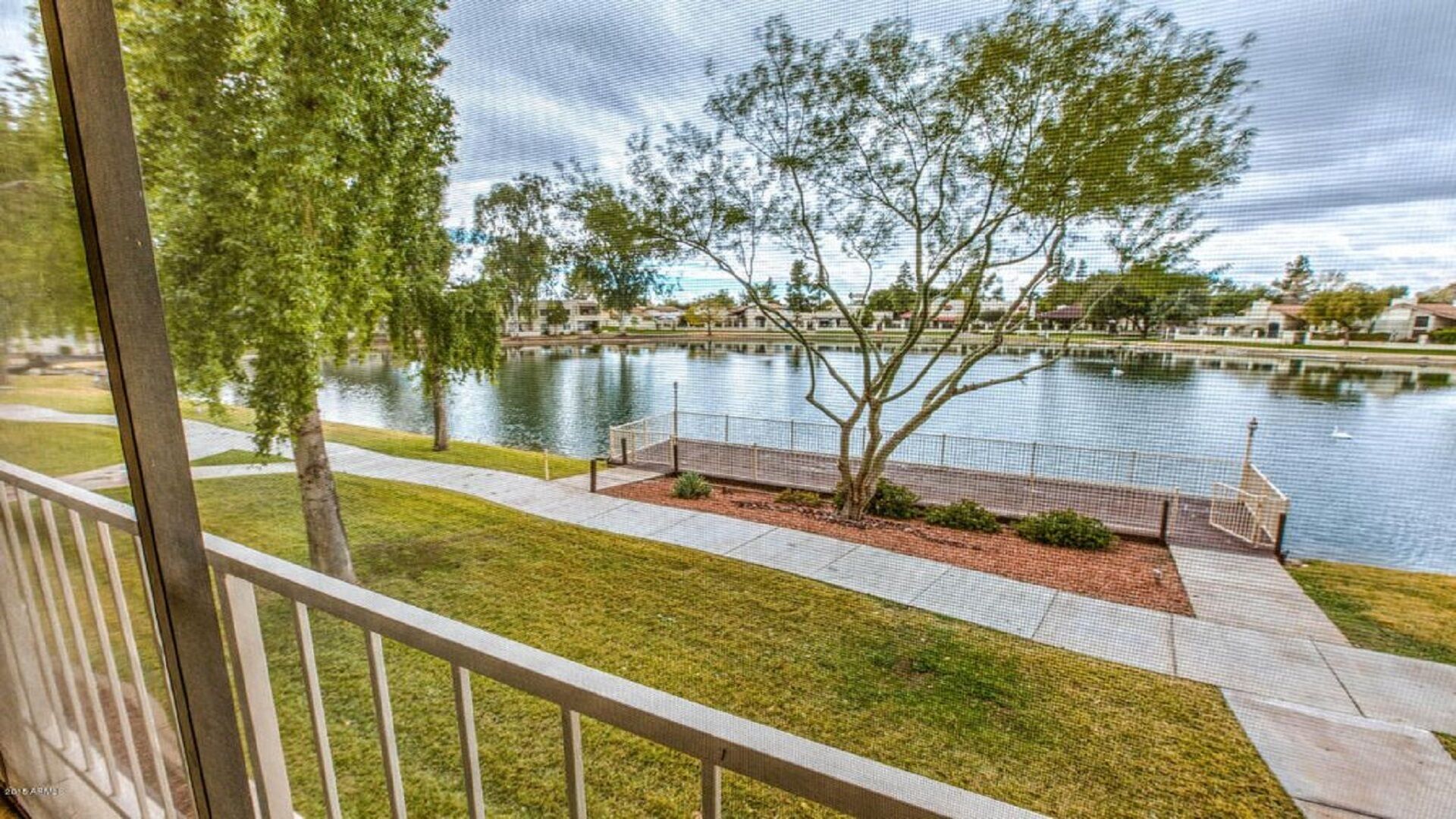 A view of a lake with a wooden deck and a grassy area in the foreground.