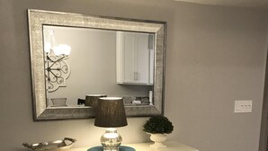 Une console blanche, avec un miroir au-dessus, une lampe et une petite plante.