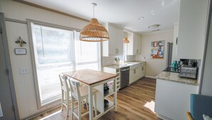 A modern kitchen with white cabinets, a wooden dining table, and a hanging light fixture.