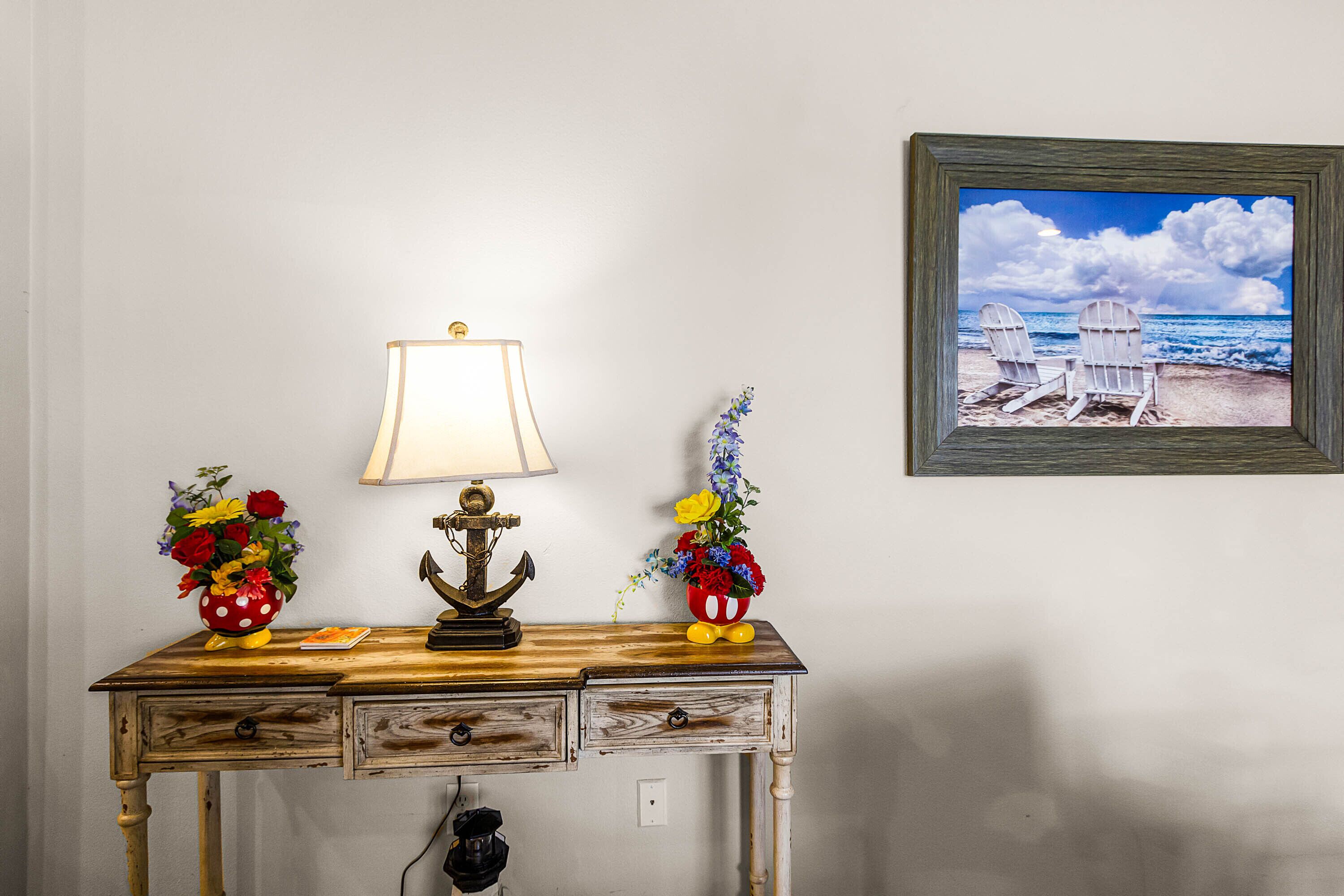 A wooden desk with a lamp, two flower vases, and a framed picture of a beach scene.