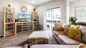Ein Wohnzimmer mit Flachbildfernseher, Holzunterhaltungseinheit, Sofa und Pouf.