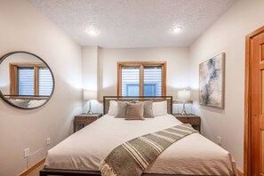 A bedroom with a bed, two bedside tables, a mirror, a window, and a painting on the wall.