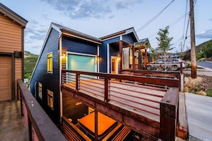 A two-story house with a visible garage door, a wooden deck, and a vehicle parked outside.