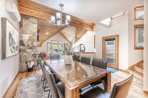 A spacious dining area with a large wooden table, stone wall, and a modern chandelier.