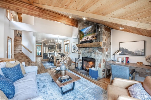 A spacious living room with a stone fireplace, a television mounted above it, and a staircase leading to another level.