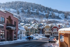 A snow-covered street in a small town with colorful houses and a mountain in the background.