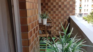 Een balkon met een bakstenen muur, een klein tafeltje met een plant in een pot en een gestreept kleed.