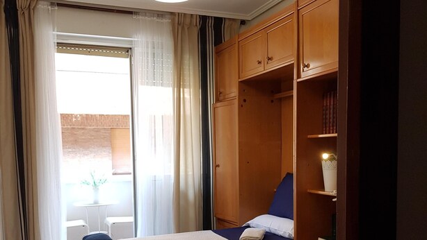 Een hotelkamer met twee bedden, een houten garderobe, een bureau met stoel en een raam met gordijnen.