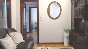 Een woonkamer met een donker leren bank, een witte salontafel met boeken, een decoratieve spiegel en een kast met glazen deuren.