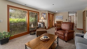 A spacious living room with a large window, a wooden coffee table, a brown leather armchair, and a grey sofa. - The Silver Cliff, 2BR Walk to Lifts and Main St! (Park City)