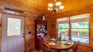 Interior de una cabaña de madera con una mesa de comedor preparada para cuatro, un aparador rojo con vajilla y una araña.